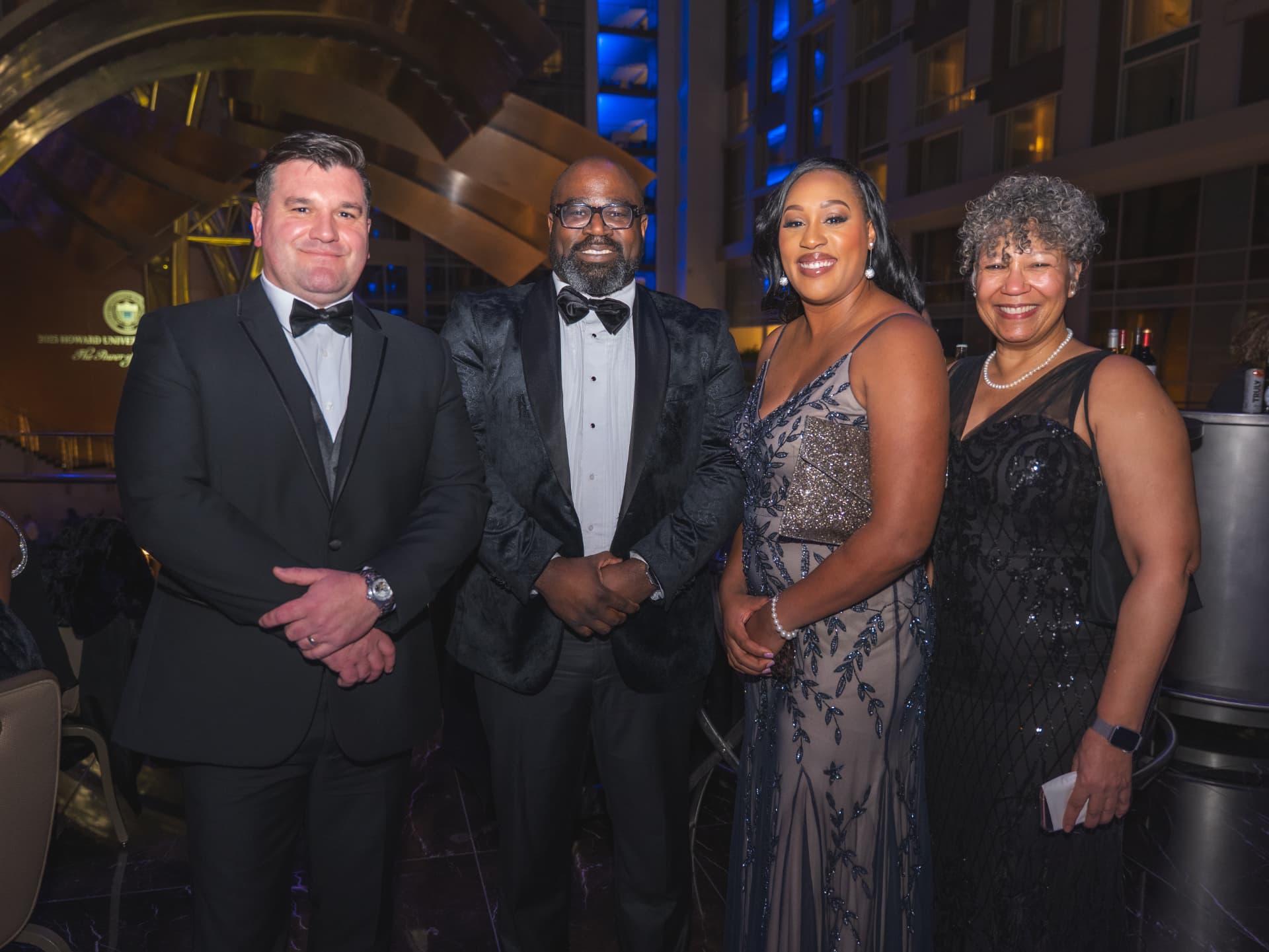 Four guests in formalwear posing together in the hotel atrium at the dinner