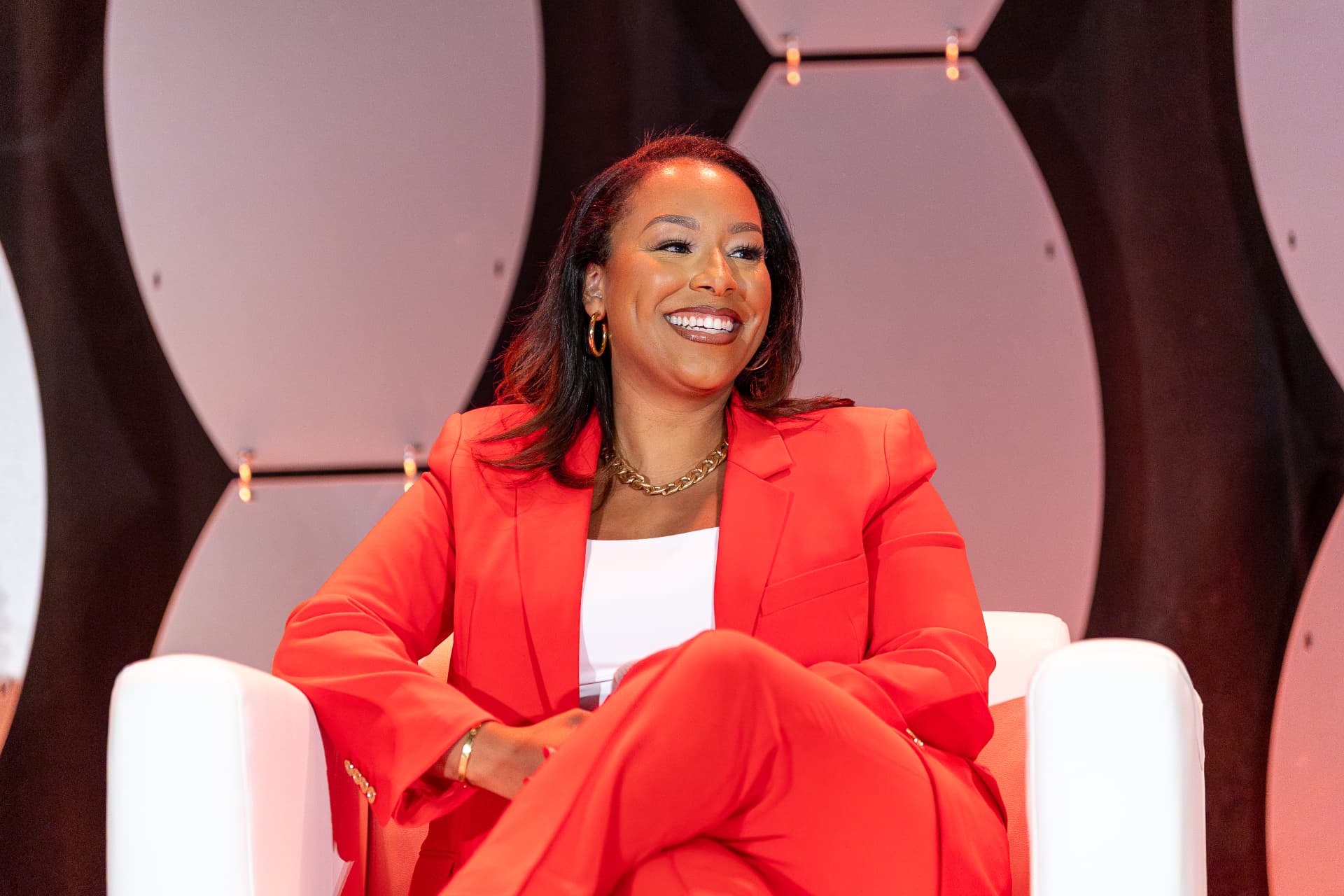Woman in a red suit laughing during a fireside conversation on stage