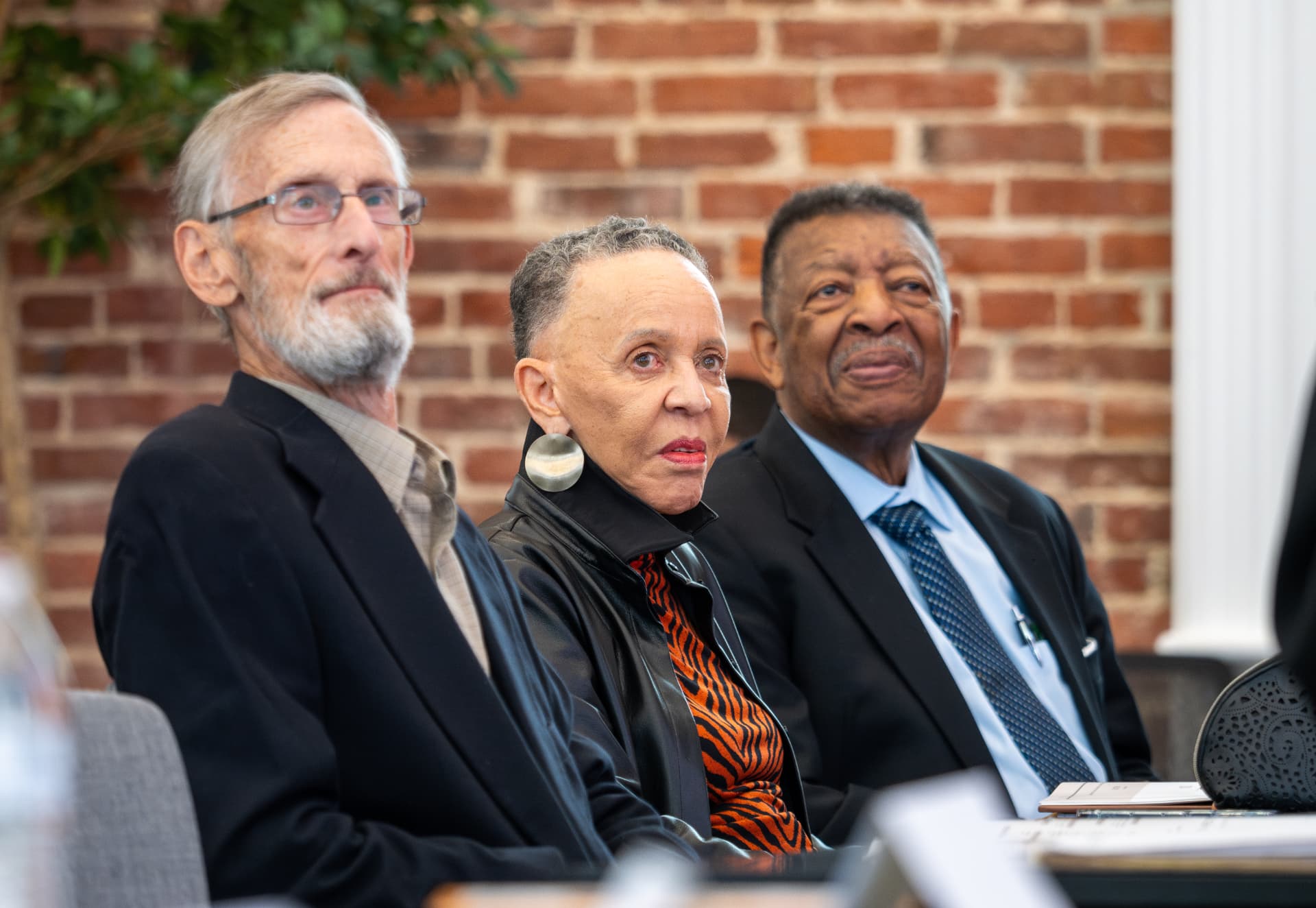Three attendees listening attentively in front of a brick wall at a conference