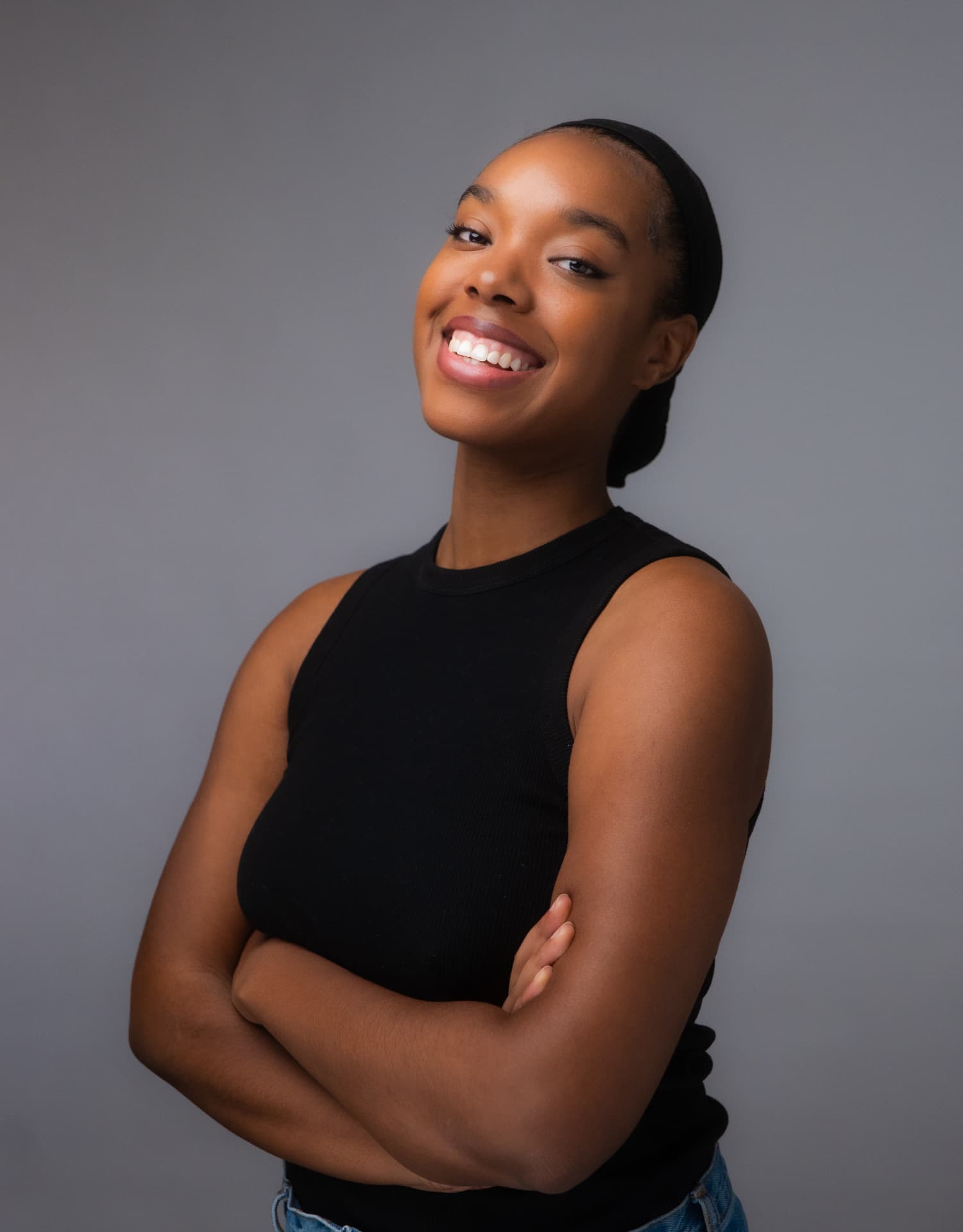 Woman in a black sleeveless top with arms crossed smiling in a studio portrait