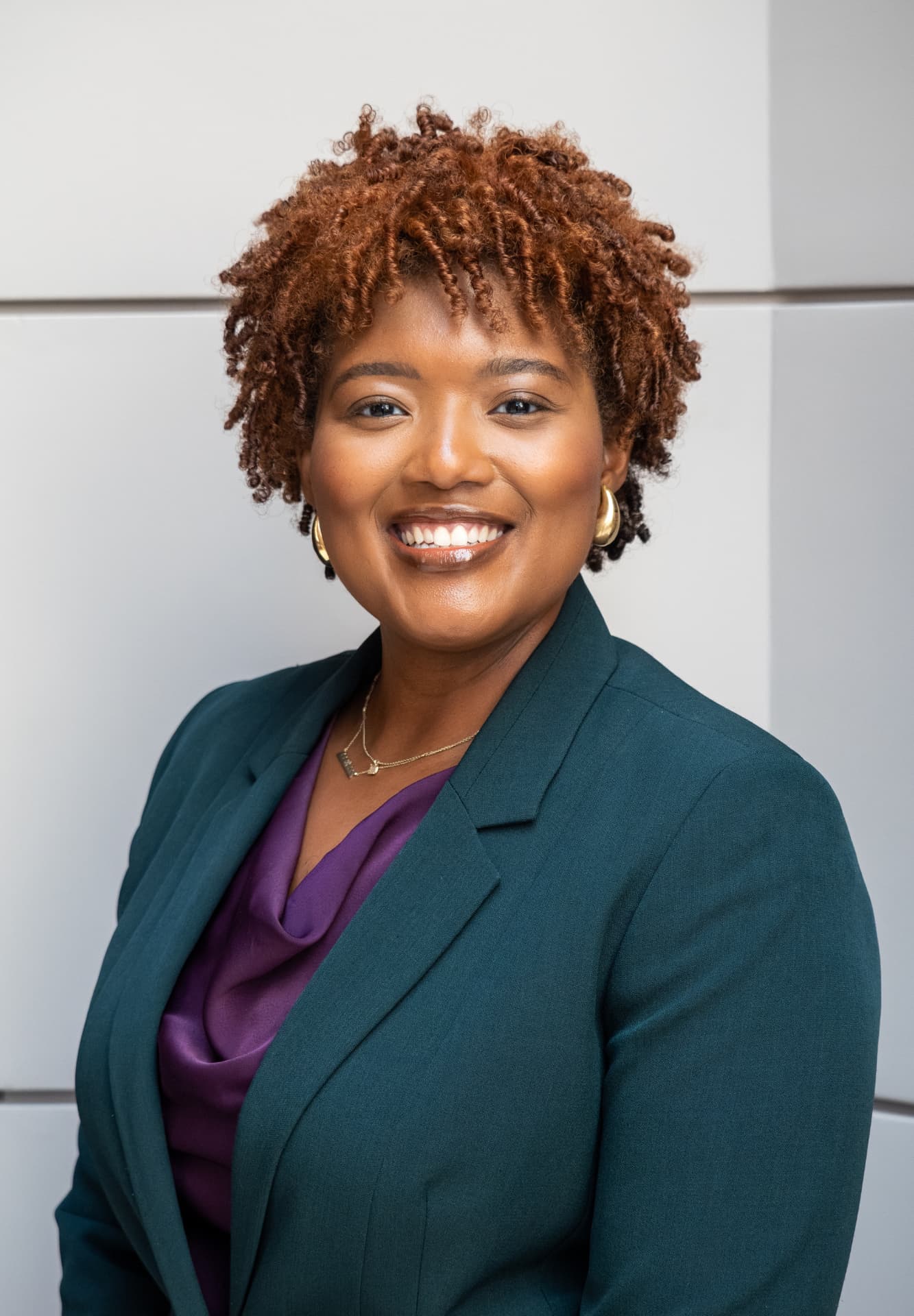 Smiling headshot of a woman with short copper curls in a green blazer and purple blouse