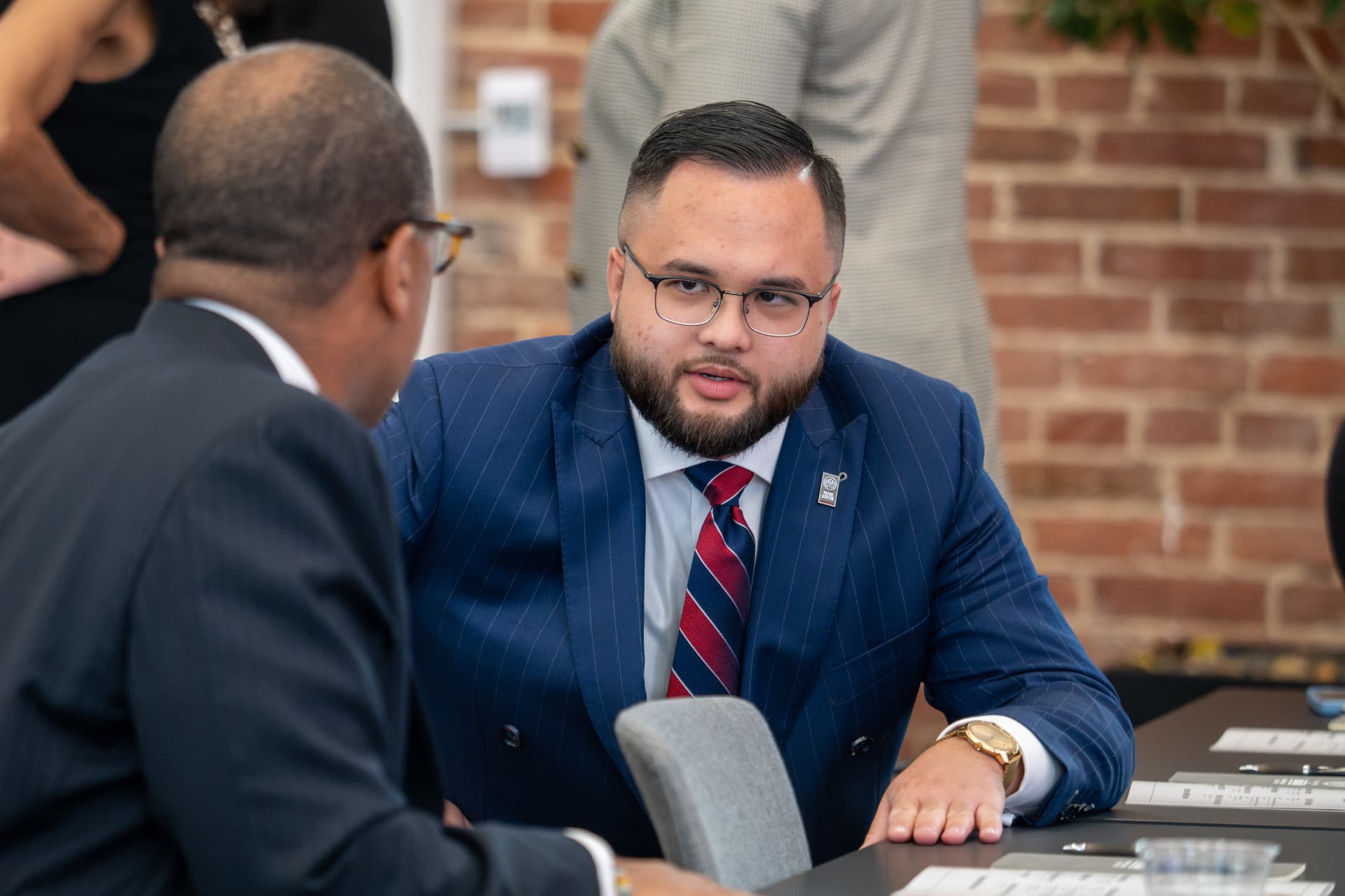 Man in a blue pinstripe suit in conversation across a conference table