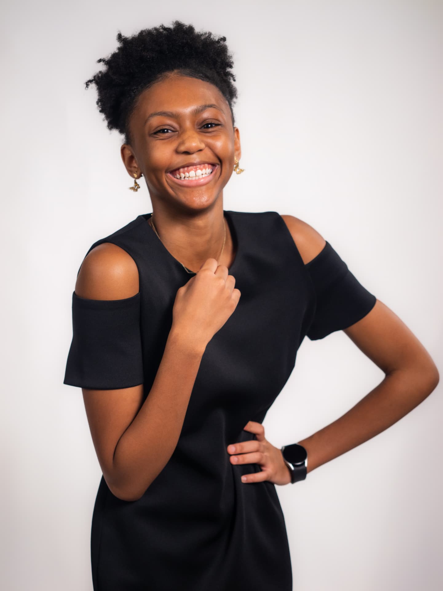 Laughing woman in a black cold-shoulder dress posing on a white studio backdrop