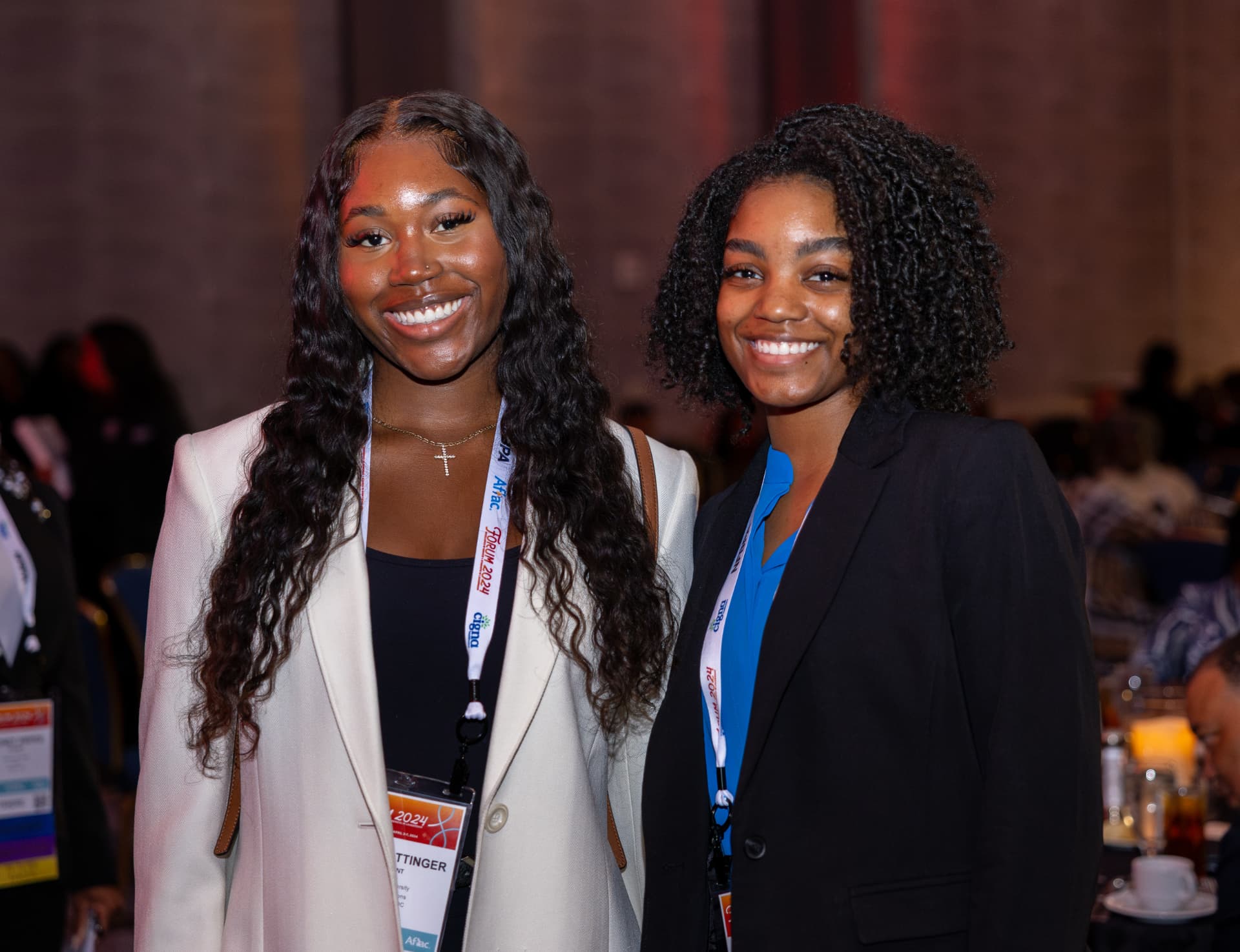Two smiling attendees posing together wearing Forum 2024 lanyards