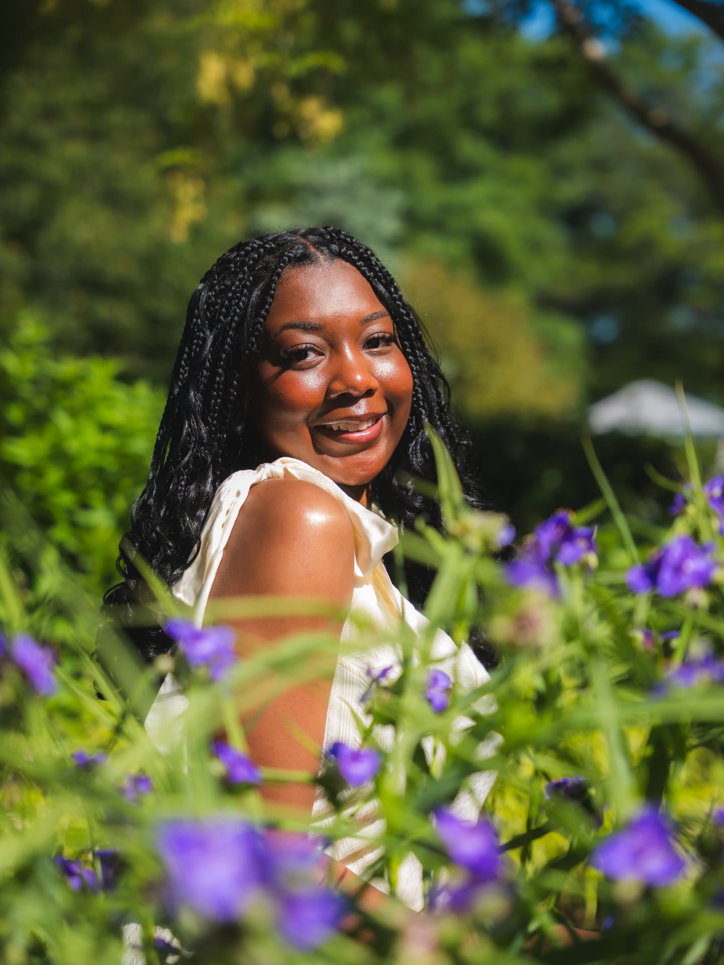 Smiling graduate in a white top standing among purple flowers in a garden