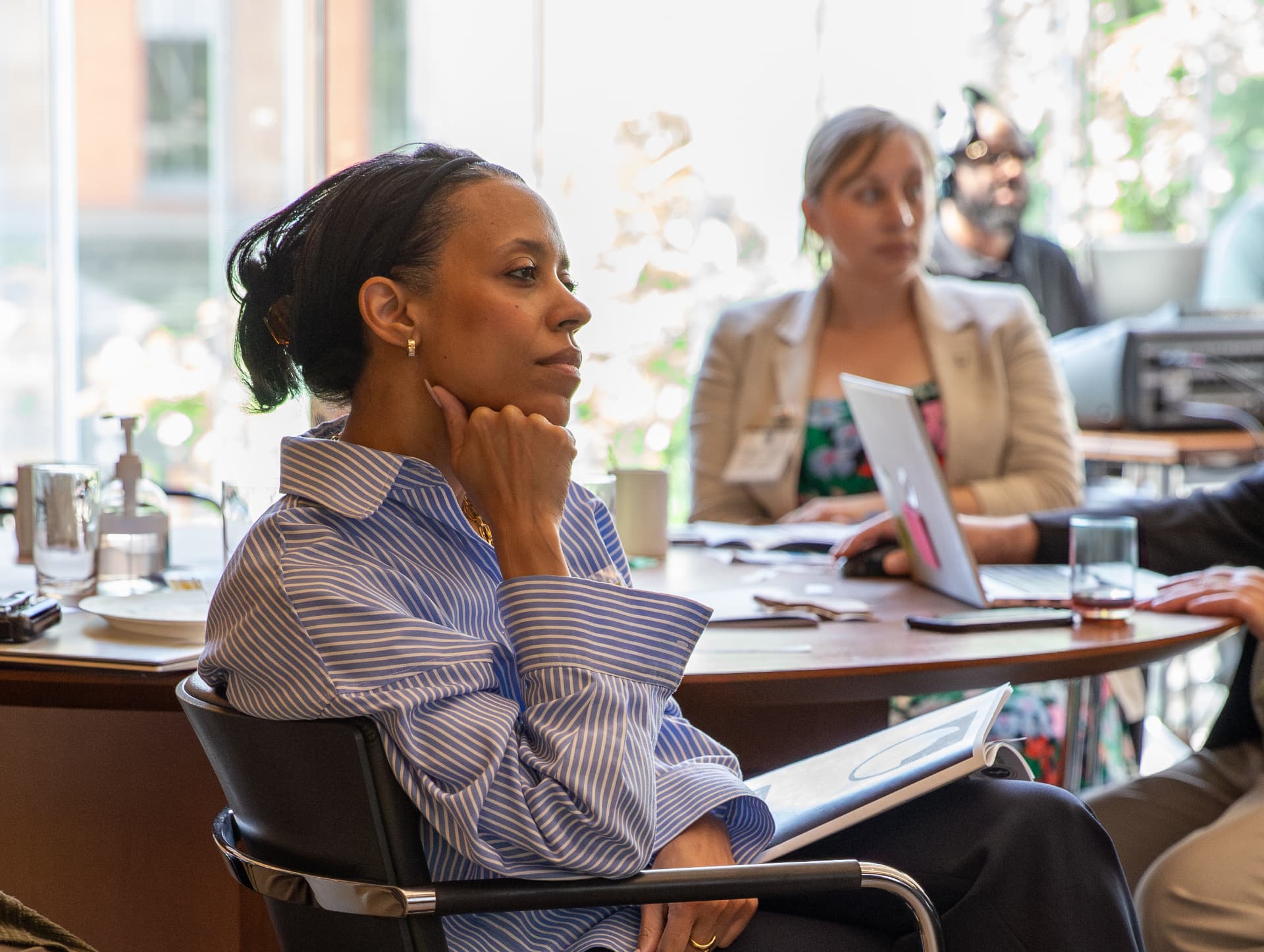 Woman in a striped shirt listening thoughtfully during a workshop table discussion