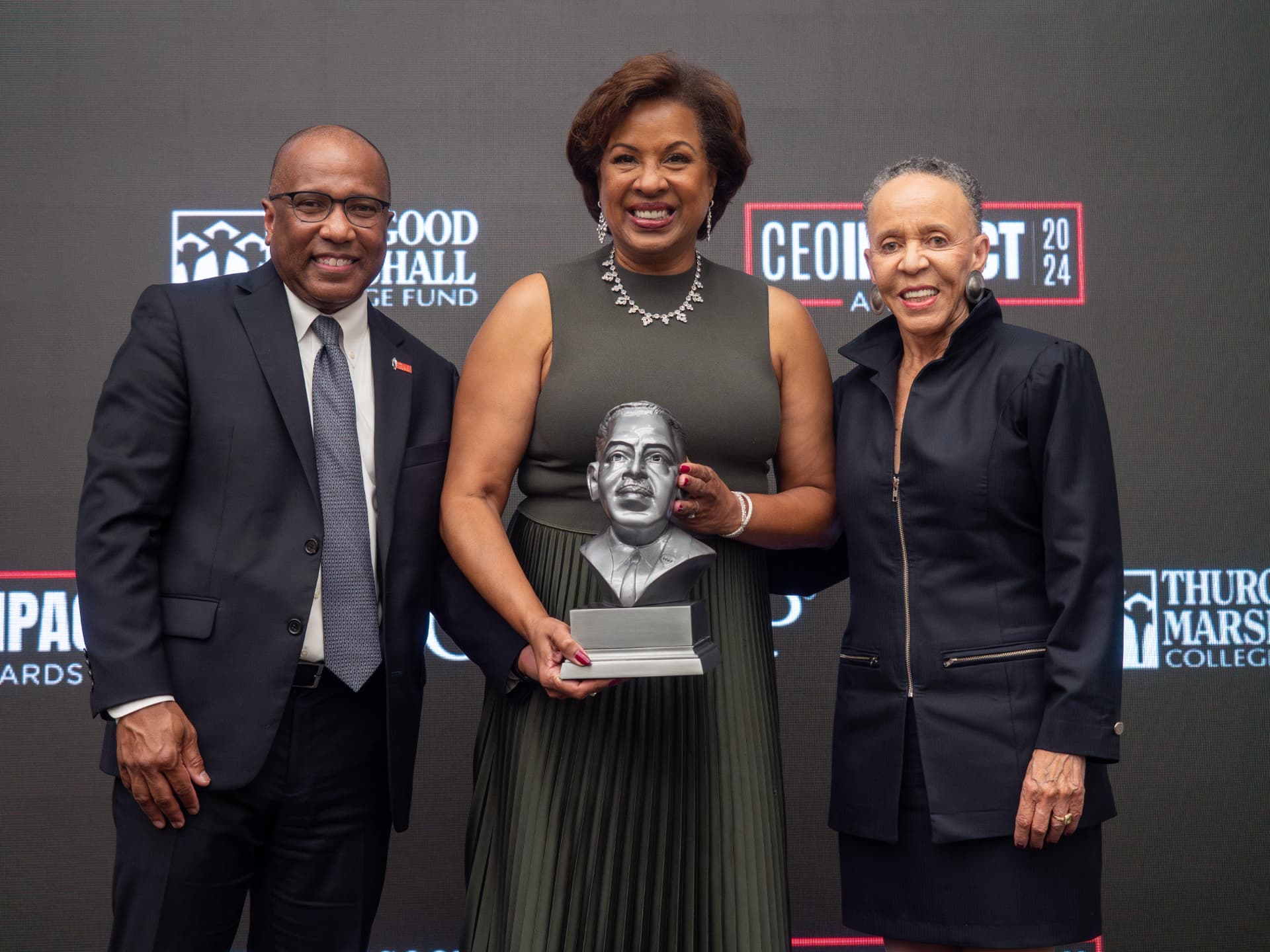 Woman in an olive dress holding a Thurgood Marshall bust award, flanked by two guests at the CEO IMPACT Awards