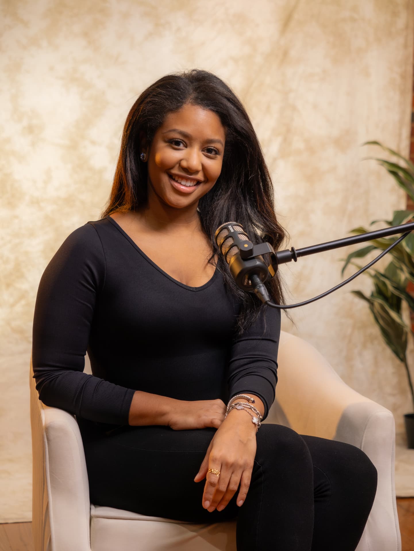 Woman in black seated in a studio chair smiling beside a podcast microphone