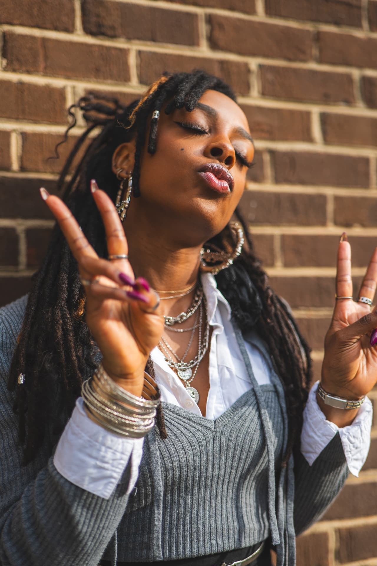 Woman with locs throwing peace signs while blowing kisses against a brick wall