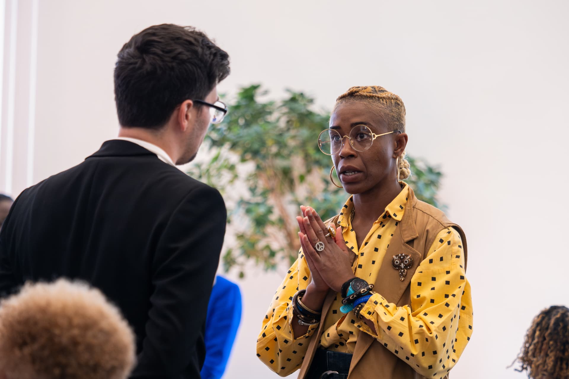 Woman in a yellow polka-dot blouse talking with a man in a black suit