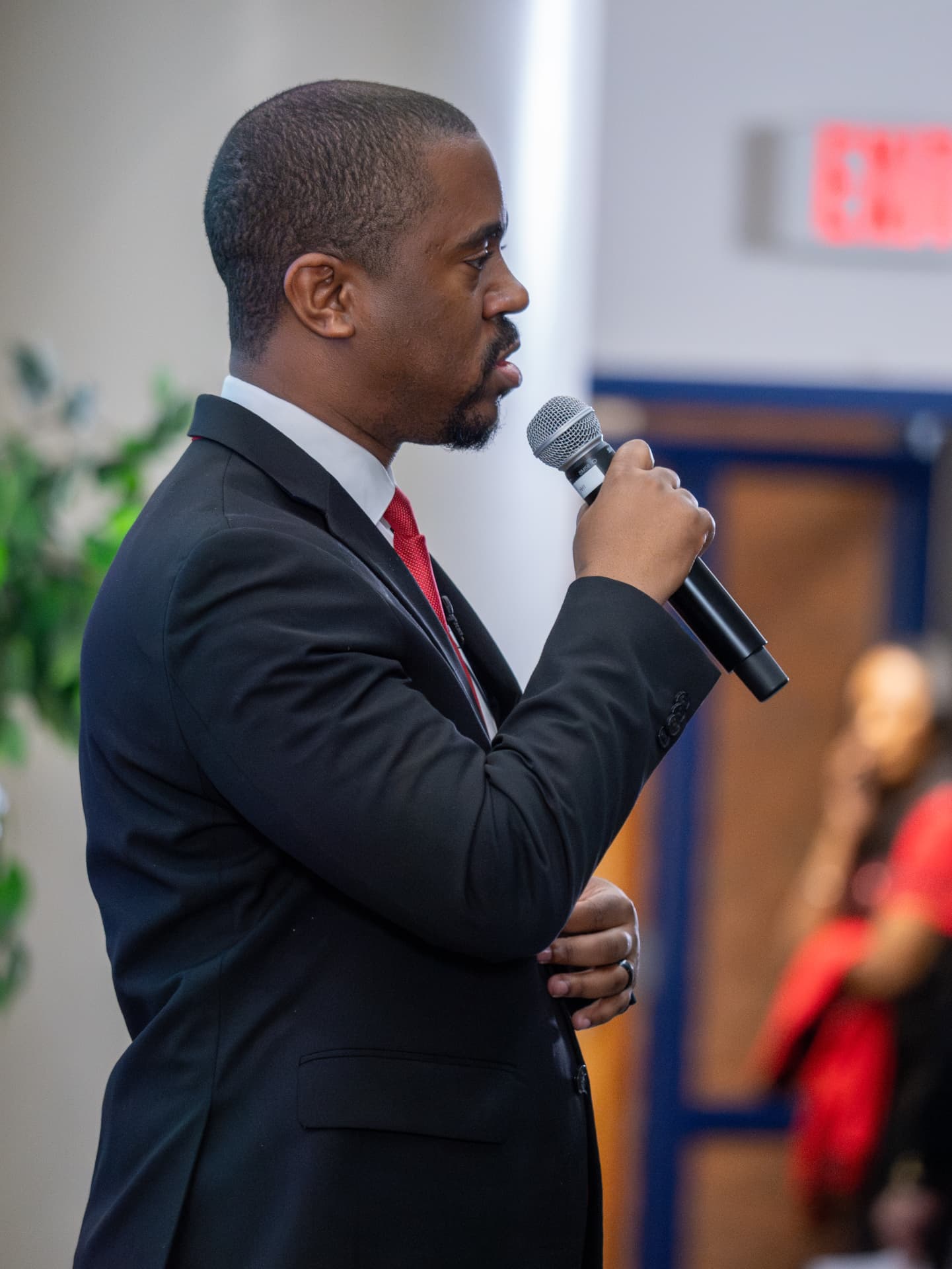 Speaker in a red tie addressing a room with a handheld microphone