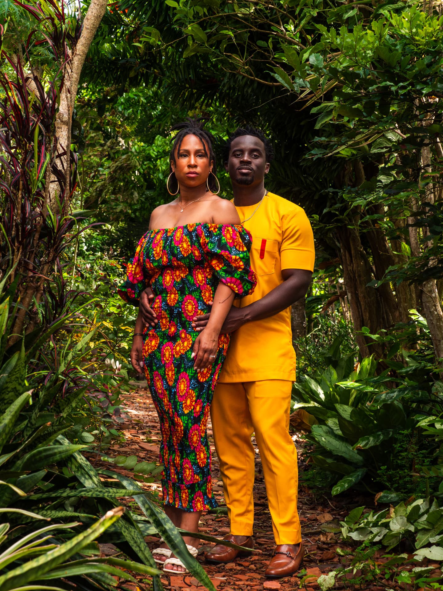 Couple in bright patterned outfits posing on a lush garden path