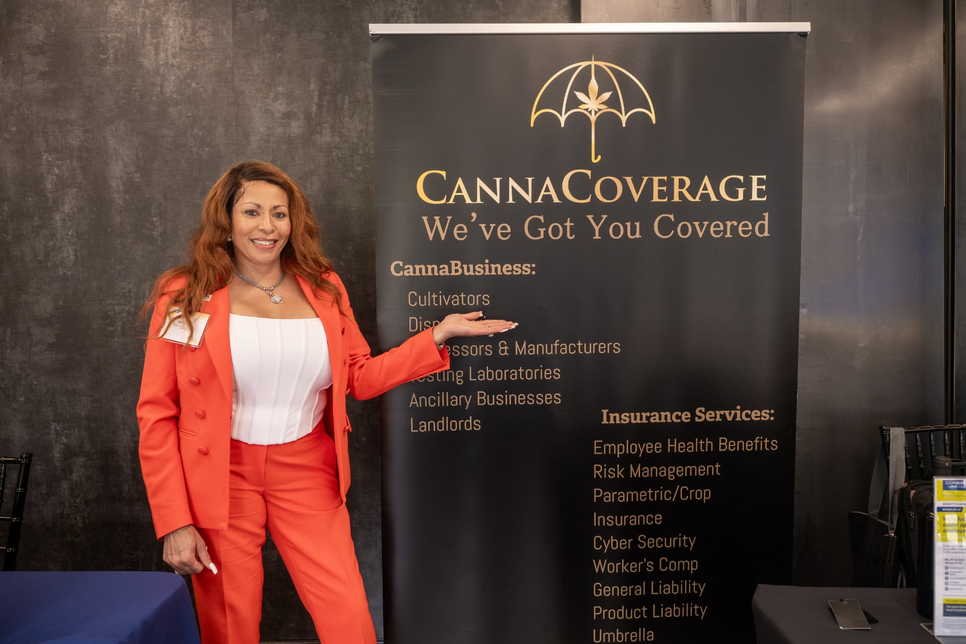 Woman in a coral suit smiling beside a CannaCoverage banner at a business expo