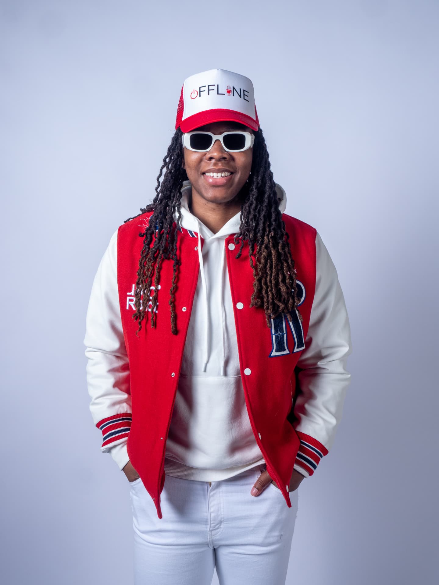 Studio portrait of a person in a red varsity jacket and white cap