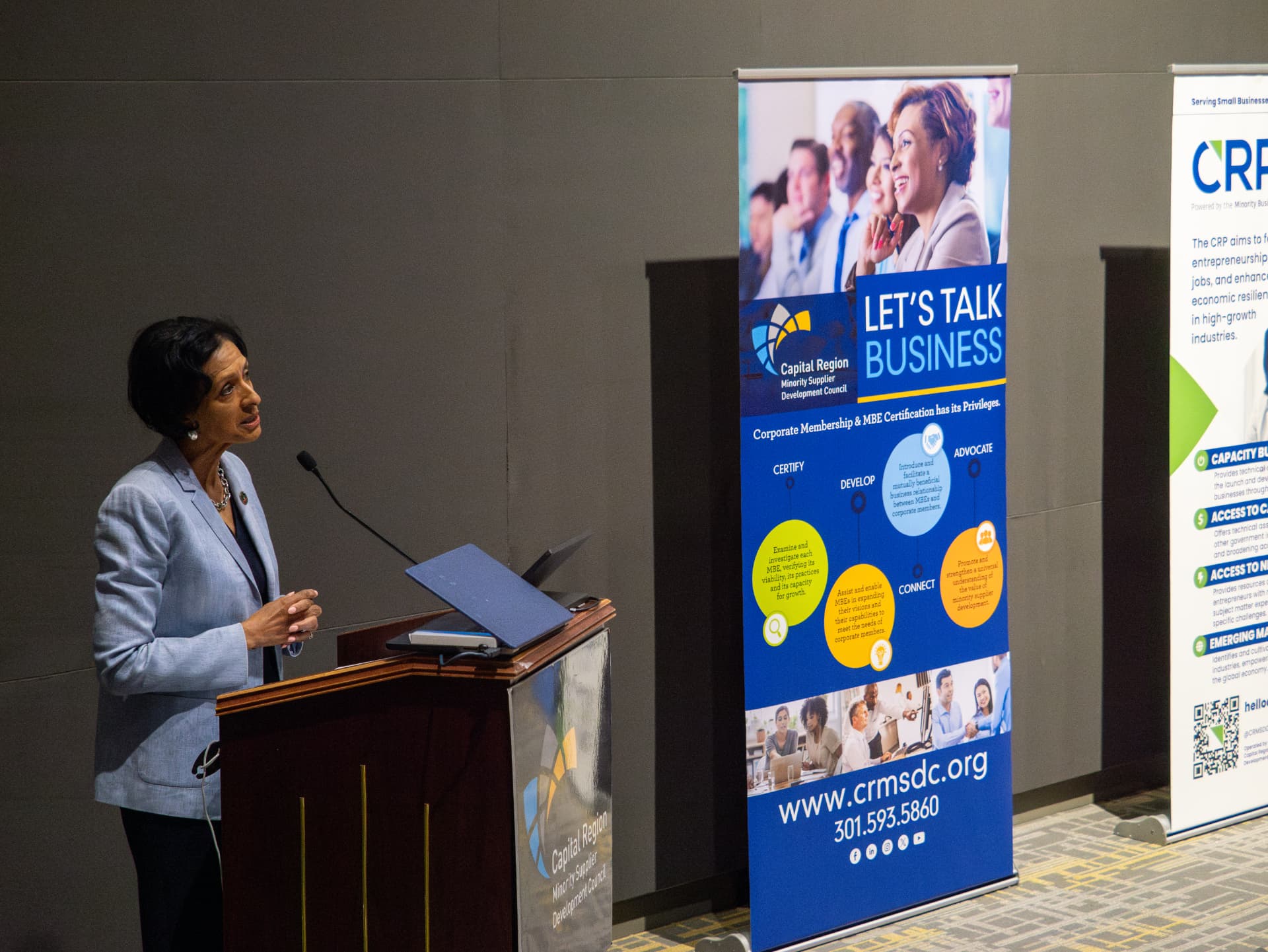 Woman in a light blazer speaking at a podium beside a Capital Region Minority Supplier Development Council banner