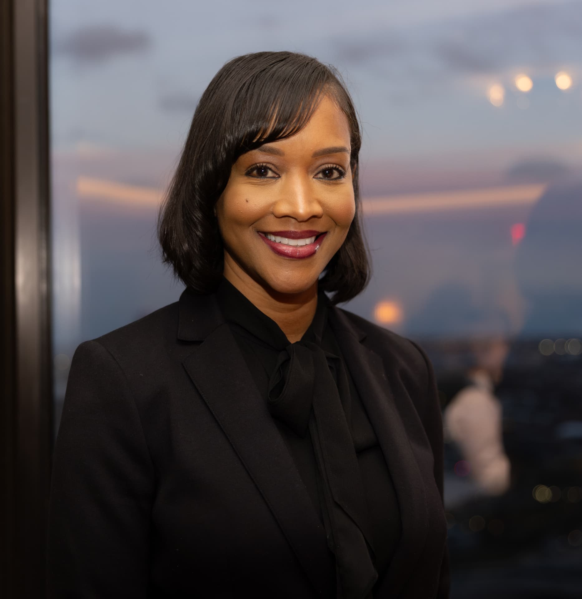 Executive portrait of a woman in a black suit by a window at dusk
