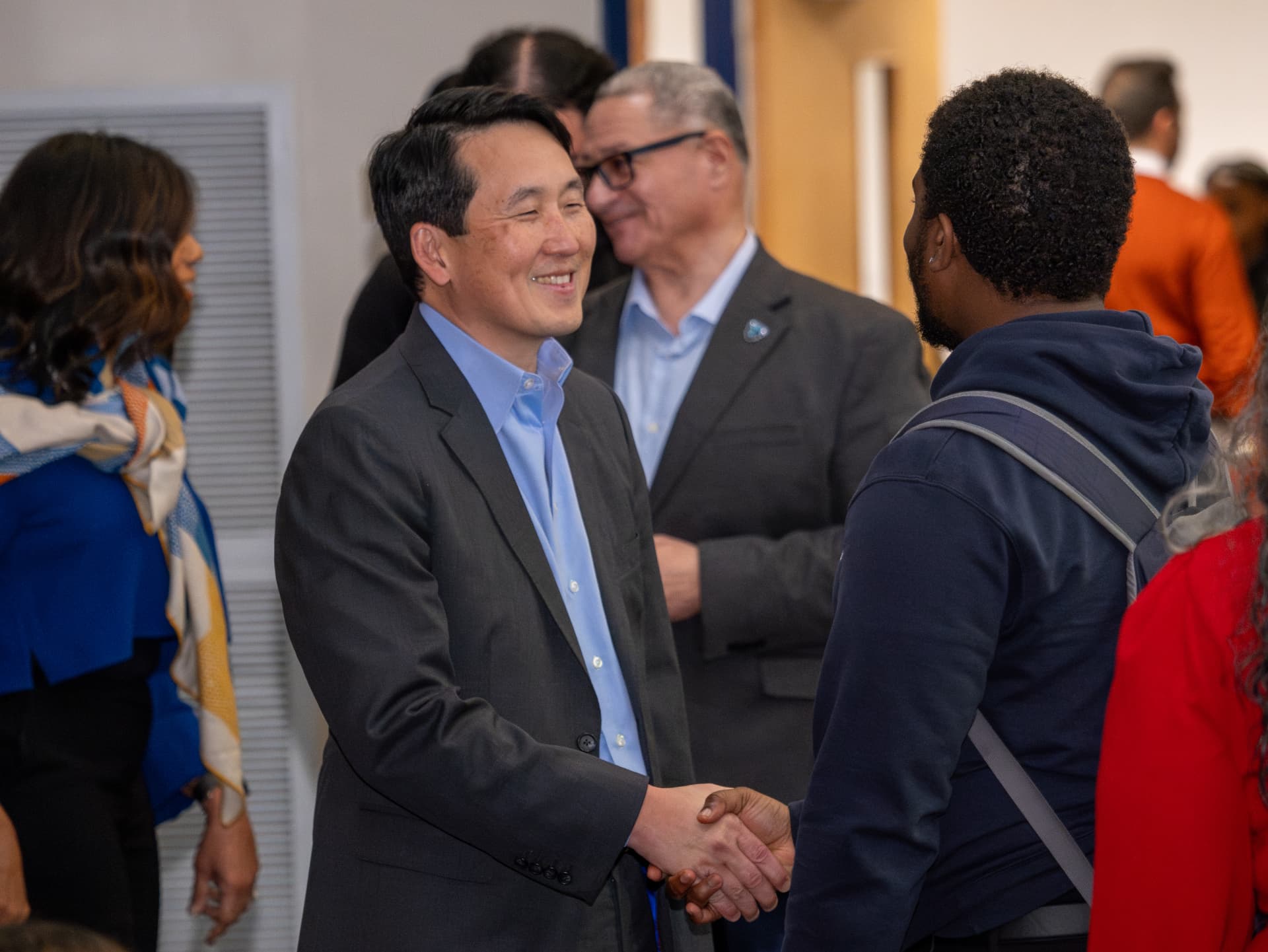 Two men in suits shaking hands and smiling at an indoor networking event